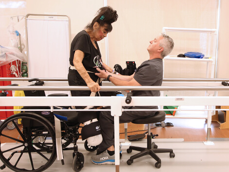 A male therapist helps his female patient to learn to walk again after amputation, utilizing the parallel bars.