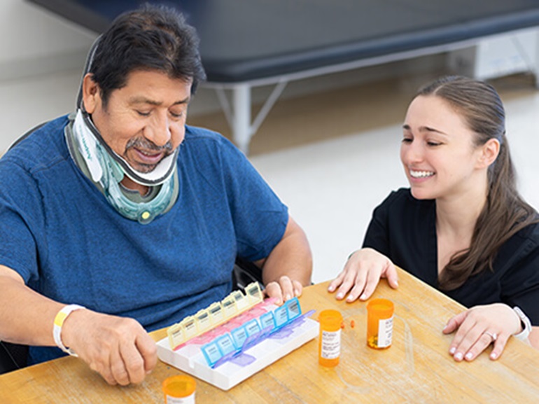 A male patient wearing a neck brace works with his occupational therapist to sort his medicine.
