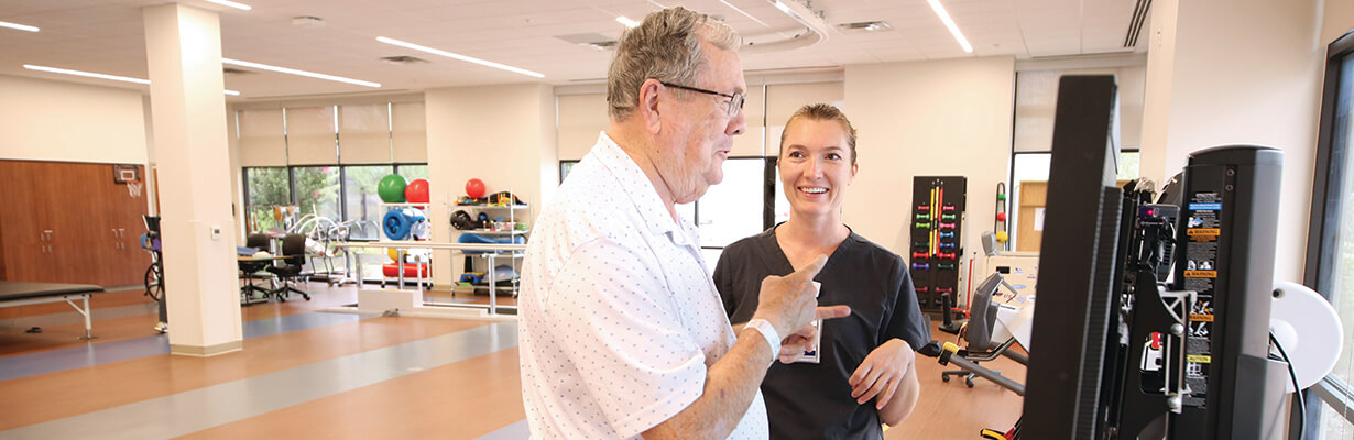 A male patient talks to their female physical therapist while at a therapy session in the hospital gym.