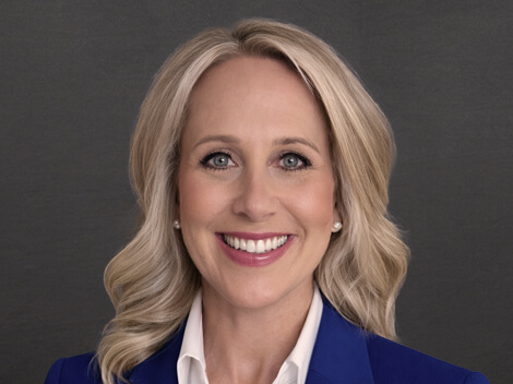 Amanda smiles at the camera with a blue blazer and curled hair.