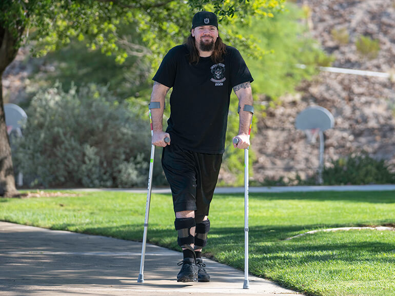 Logan using forearm braces and walking outside on a sunny day.