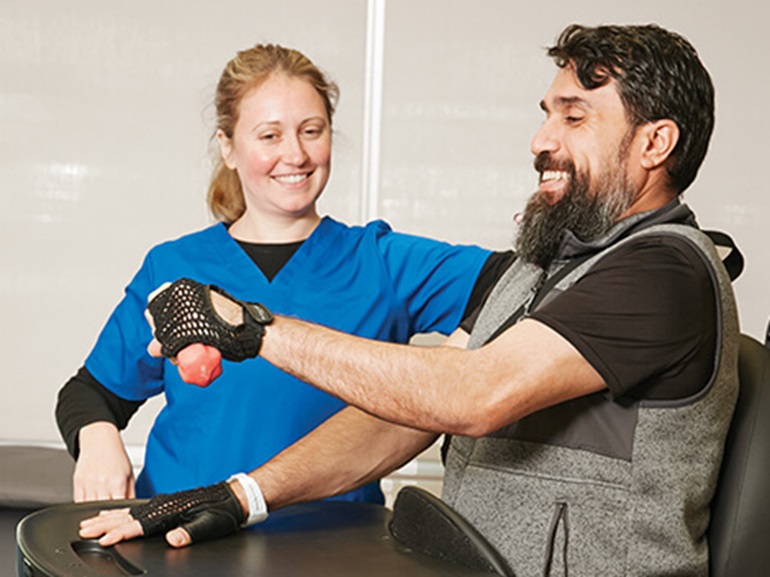 A male patient works on arm strength with his physical therapist after injury.