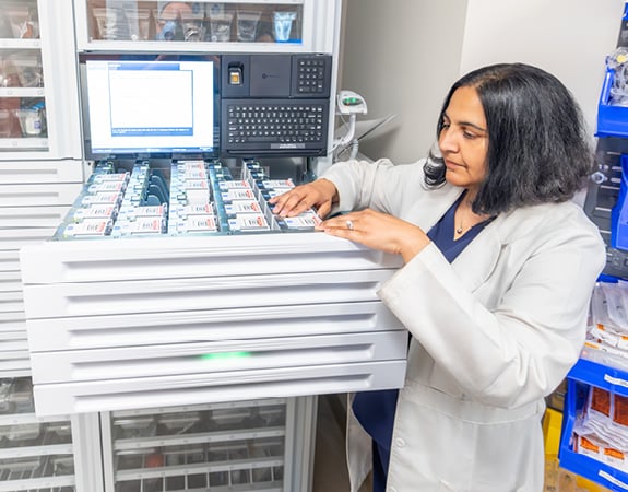 A pharmacist accesses medicine for a patient from a secured drawer.