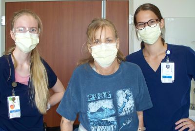 Linda stands in a critical illness hospital room with her therapists.