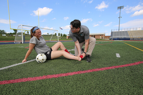 Injured female soccer player sitting on the field with her trainer.